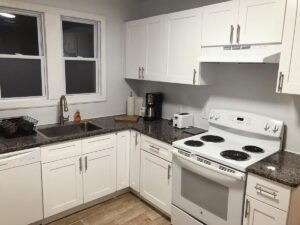Photograph of modern white kitchen with granite countertops, electric stove, coffee maker and large windows in the fully furnished unit for rent to traveling nurses in Johnson city