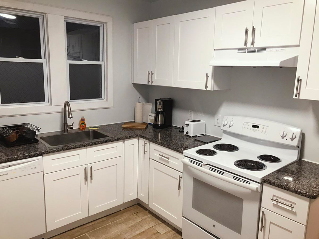 Photograph of modern white kitchen with granite countertops, electric stove, coffee maker and large windows in the fully furnished unit for rent to traveling nurses in Johnson city
